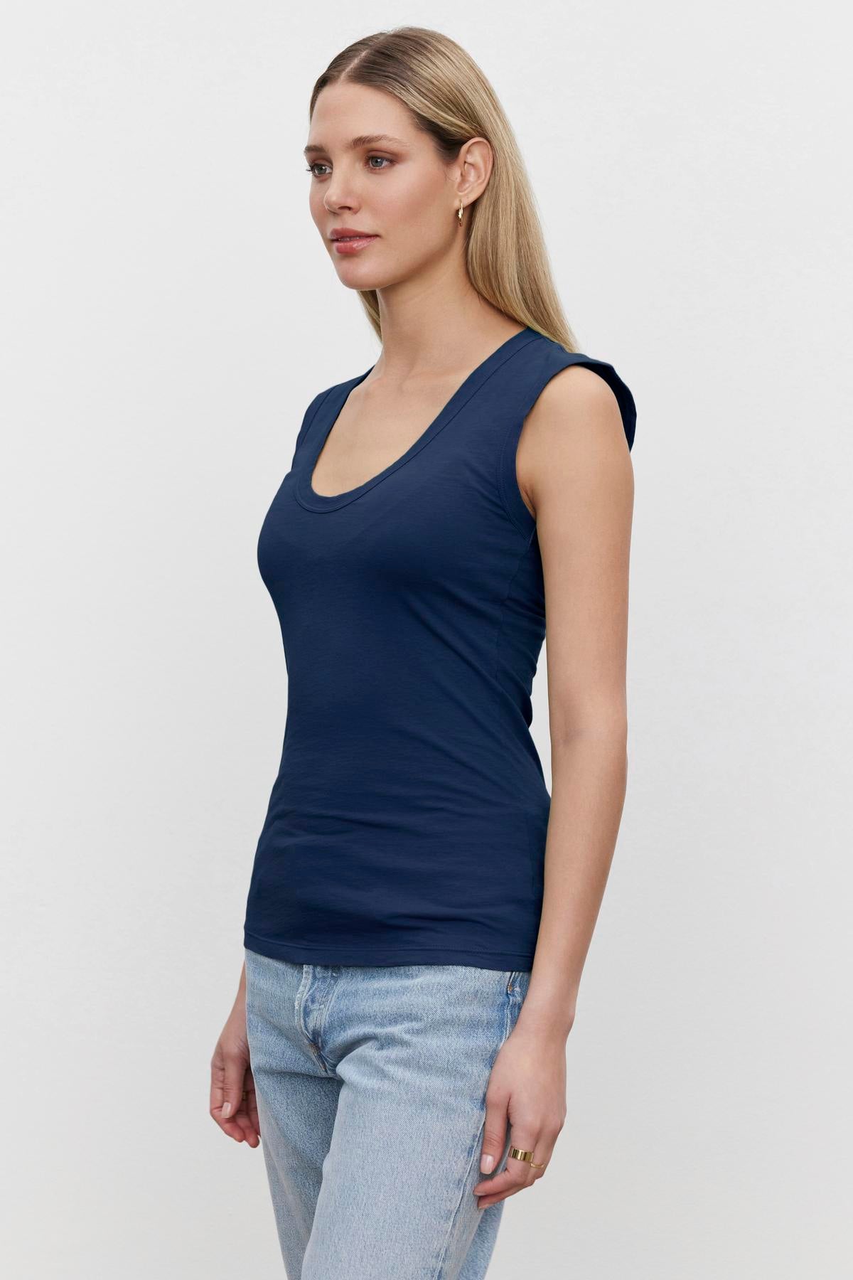 A woman wearing a Velvet by Graham & Spencer ESTINA GAUZY WHISPER FITTED TANK TOP and jeans with a low-scoop-neck.-36273869619393