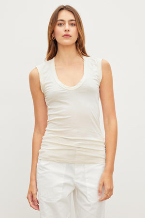 The model is wearing white pants and a ESTINA GAUZY WHISPER FITTED TANK TOP in cream by Velvet by Graham & Spencer with a low-scoop-neck.
