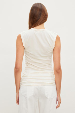 The woman is wearing a white ESTINA GAUZY WHISPER FITTED TANK TOP and white pants, showing off the back view. (Brand Name: Velvet by Graham & Spencer)