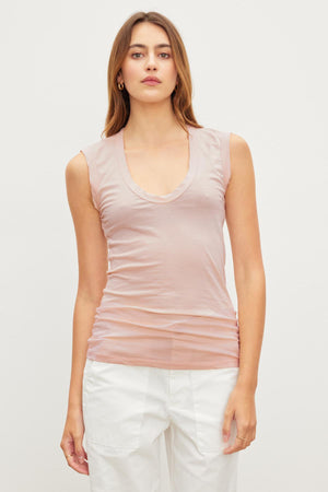 A woman wearing the ESTINA TANK TOP by Velvet by Graham & Spencer in soft pink stands against a plain background paired with white pants.