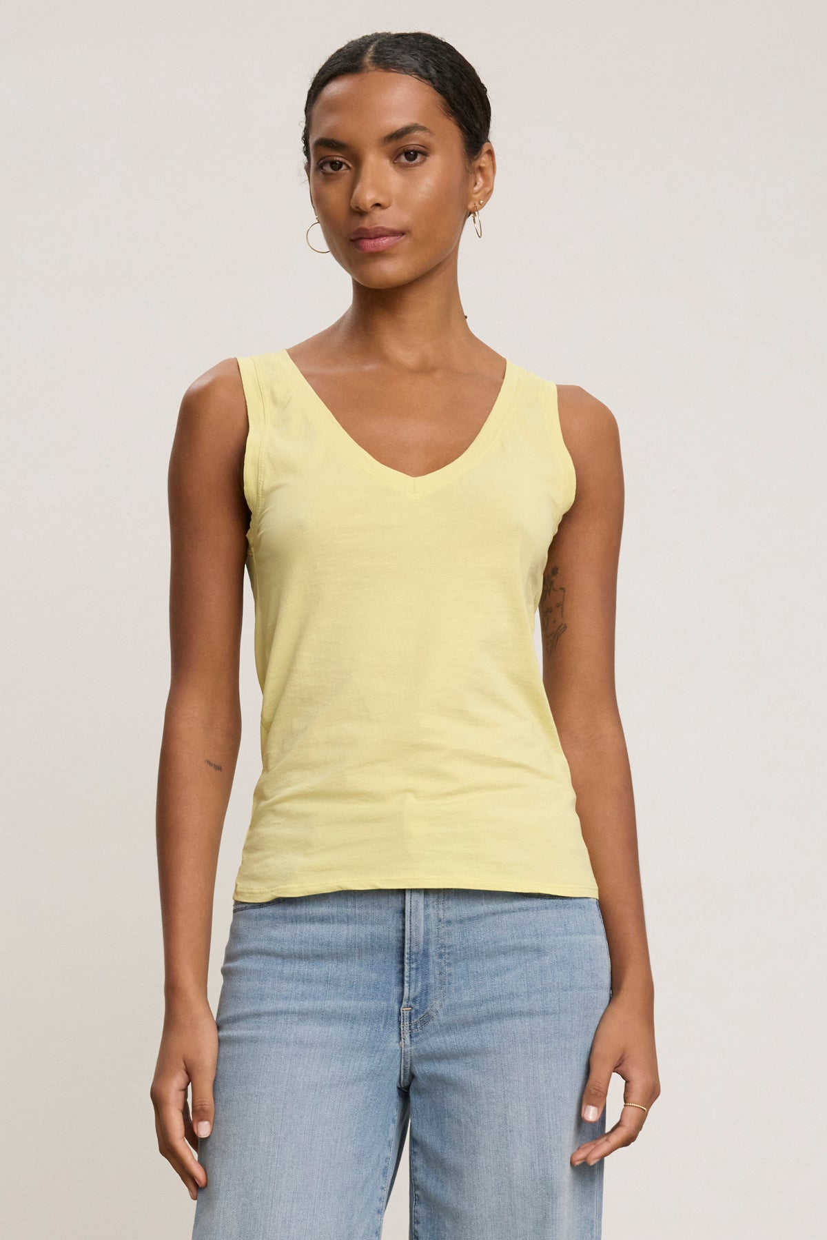 A woman models the EVELYN TANK TOP by Velvet by Graham & Spencer—a light yellow, sleeveless V-neck piece—paired with light blue jeans against a plain background, highlighting its versatility as a wardrobe essential.-39079877968065