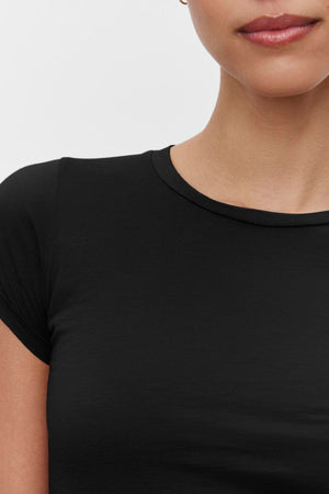 A cropped image of a person wearing the JEMMA TEE, a timeless staple by Velvet by Graham & Spencer, against a white background, showing from the lips to the upper chest.