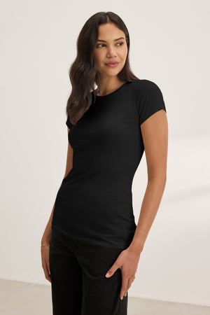 A woman in the JEMMA TEE by Velvet by Graham & Spencer, a fitted black crew neck, paired with matching black pants, stands against a plain light background, looking slightly to her left.