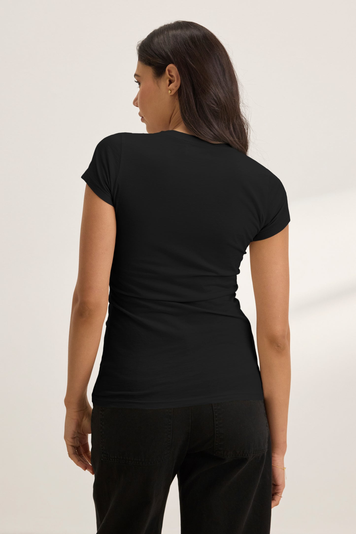A woman with long dark hair stands facing away, wearing the JEMMA TEE by Velvet by Graham & Spencer in black with matching black pants, set against a neutral background.-40183209361601