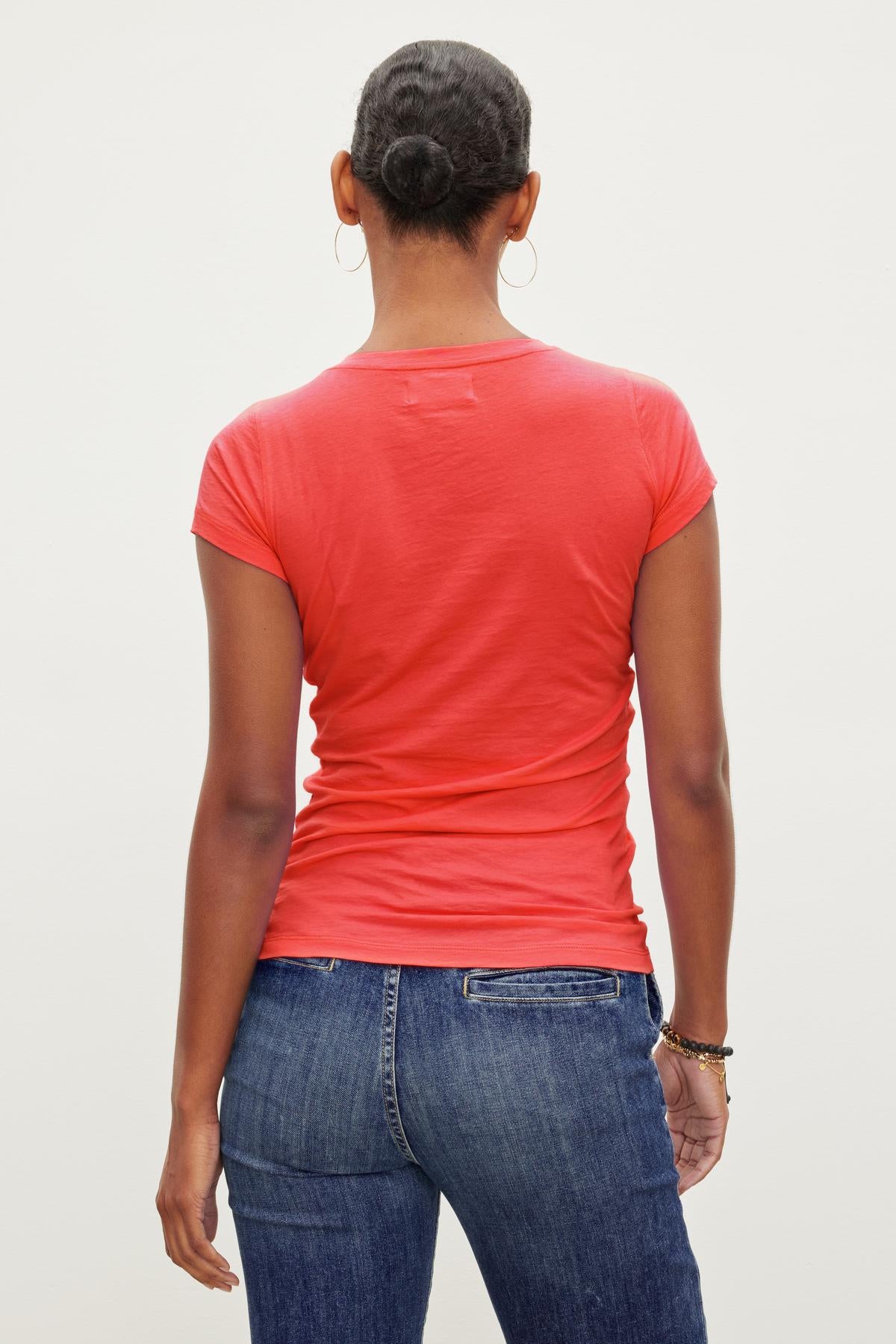   The back view of a woman wearing a red t-shirt and jeans, jazzing up her look with an Velvet by Graham & Spencer JEMMA GAUZY WHISPER FITTED CREW NECK TEE. 