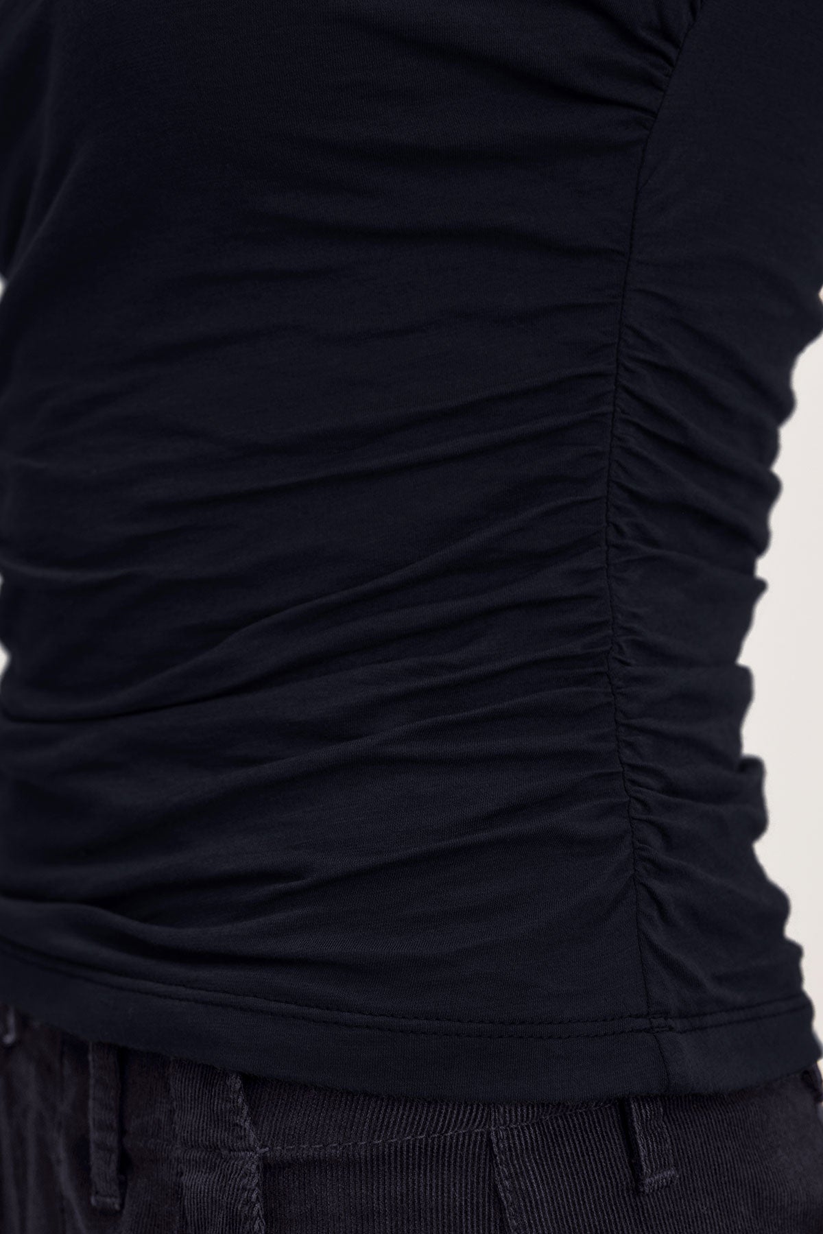   Close-up of a person wearing the MADELINE TANK TOP by Velvet by Graham & Spencer paired with dark pants, highlighting the side detail of the gathered fabric and achieving a fitted look. 