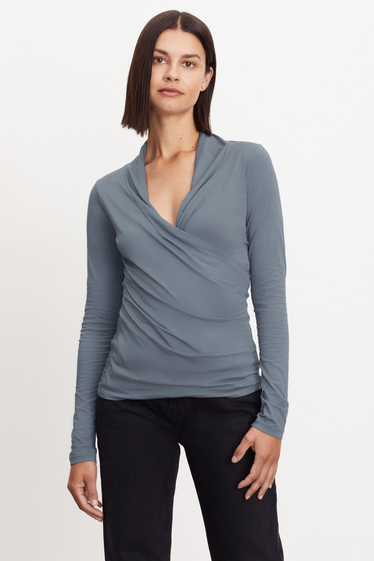 The model is wearing a Velvet by Graham & Spencer MERI WRAP FRONT FITTED TOP gray long-sleeved top with cross-over v-neck.-36094410588353