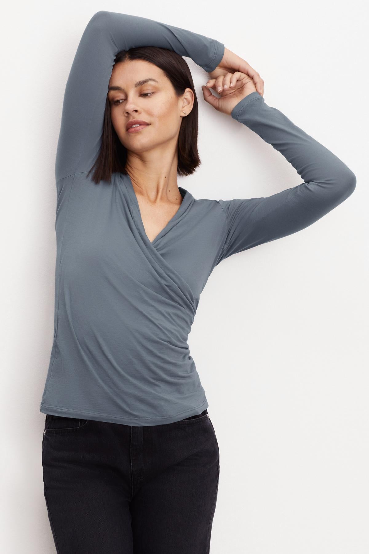   A woman wearing a Velvet by Graham & Spencer MERI WRAP FRONT FITTED TOP, a fitted, grey long-sleeved top with a cross over v-neck. 