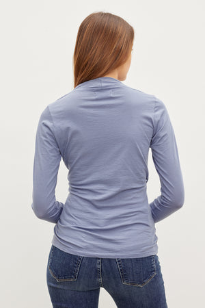 The back view of a woman wearing jeans and a blue long-sleeved MERI WRAP FRONT FITTED TOP by Velvet by Graham & Spencer with clean lines.