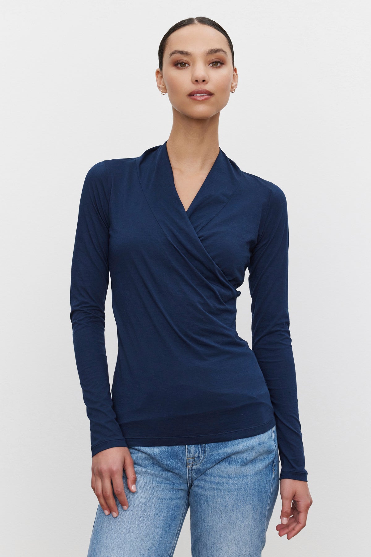   A person wearing a navy blue long-sleeved MERI TEE by Velvet by Graham & Spencer and blue jeans stands against a white background. 