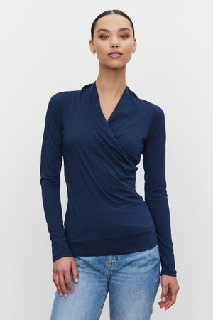 A person wearing a navy blue long-sleeved MERI TEE by Velvet by Graham & Spencer and blue jeans stands against a white background.