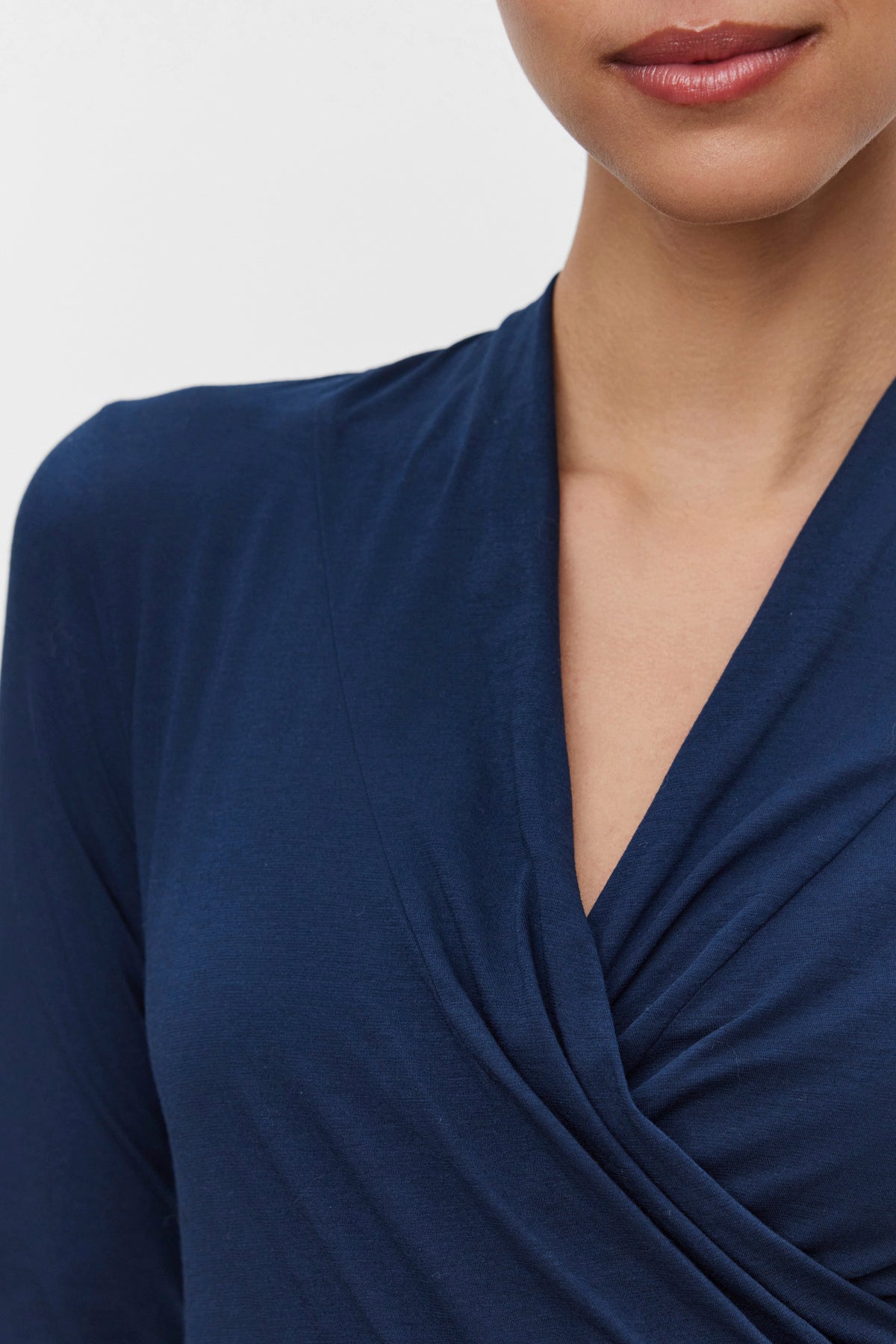   A person wearing the MERI TEE by Velvet by Graham & Spencer, a dark blue wrap-style top with a cross-over wrap detail, highlighting the V-neckline and upper shoulder. 