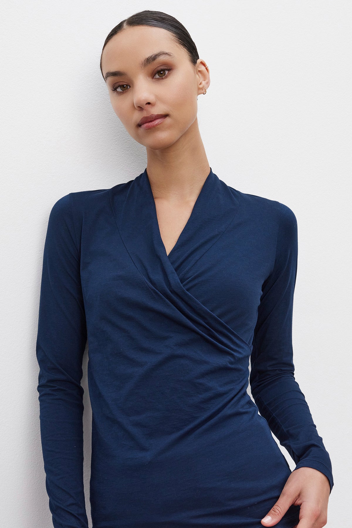   A person wearing the MERI TEE by Velvet by Graham & Spencer, a navy blue long-sleeve wrap-top with a flattering V-neckline, stands against a white background. 