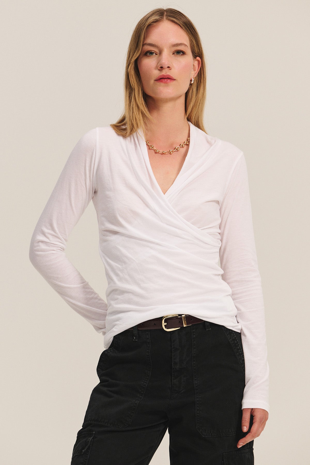 A woman stands against a plain light background wearing the MERI TEE by Velvet by Graham & Spencer, styled with black pants and a gold chain necklace.-39782436864193