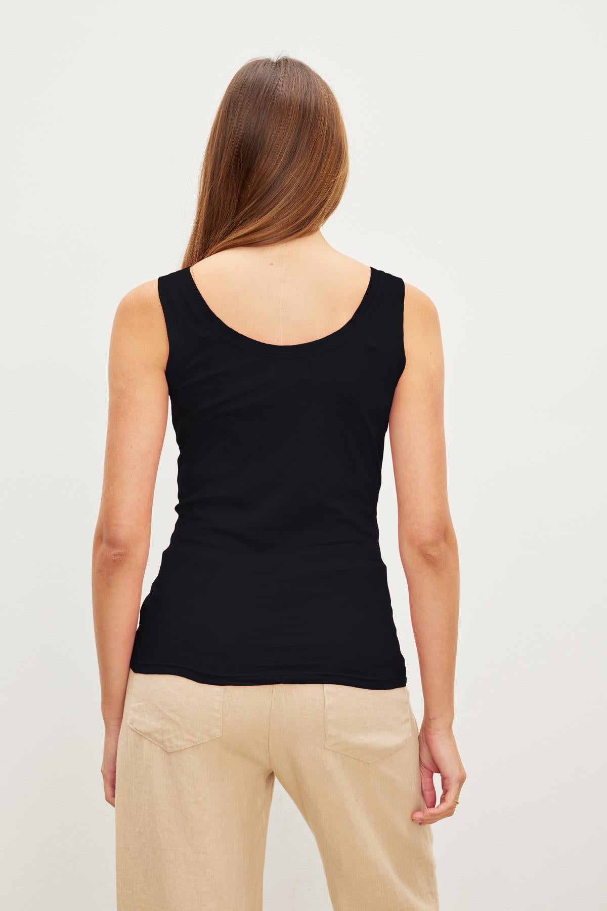 Rear view of a woman with straight brown hair wearing a Velvet by Graham & Spencer Mossy Gauzy Whisper Fitted Tank and beige pants, standing against a white backdrop.-36454076612801