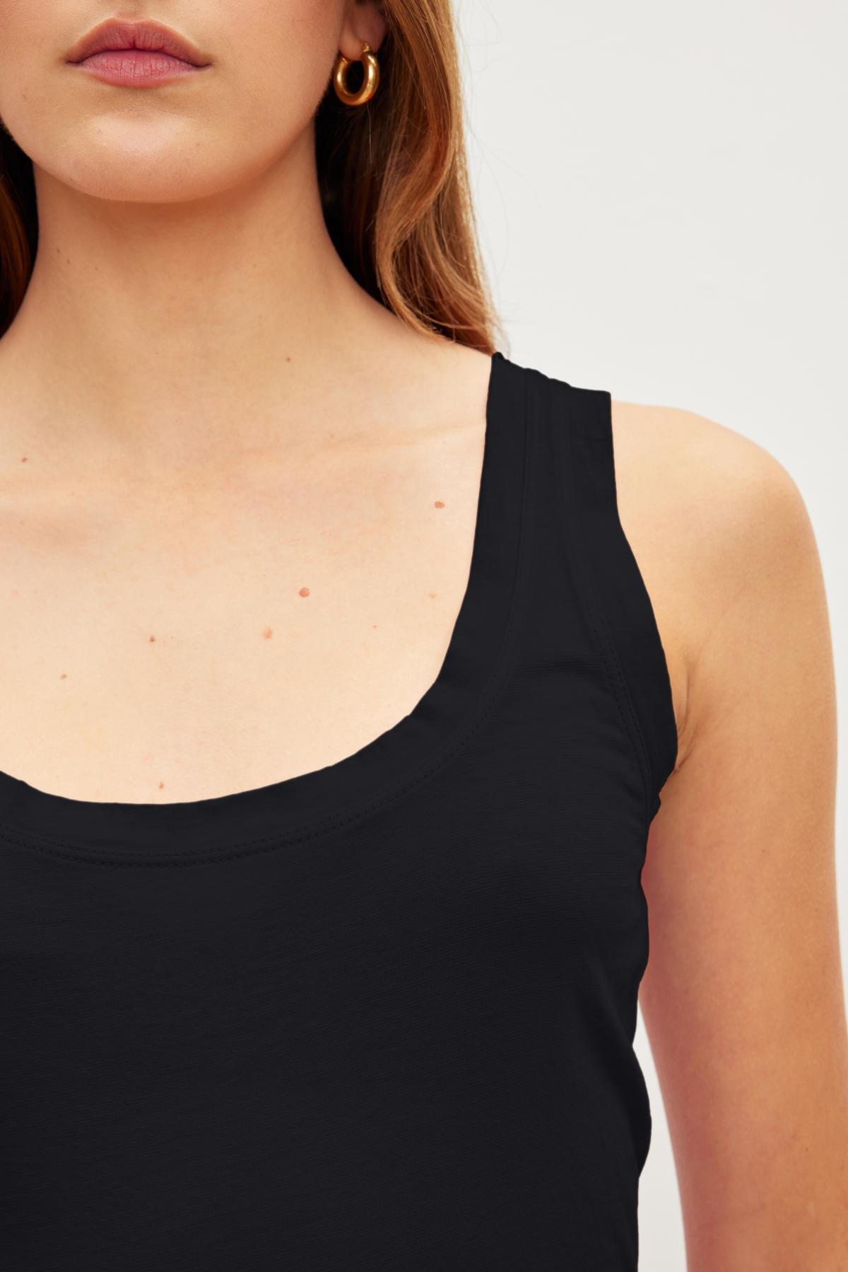 Close-up of a woman wearing a black Velvet by Graham & Spencer MOSSY GAUZY WHISPER FITTED TANK, focusing on her neck and shoulder area with visible moles.-36454076514497