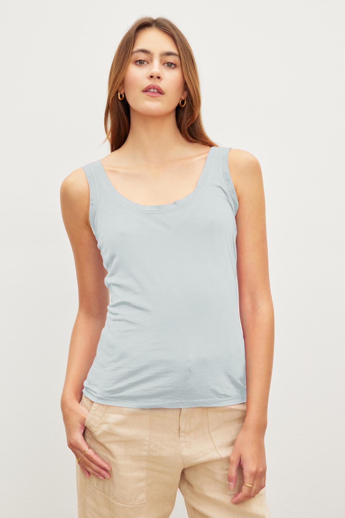 A woman with long brown hair wears a light grey gauzy MOSSY TANK TOP by Velvet by Graham & Spencer and beige pants, standing against a plain white background.-37241163186369