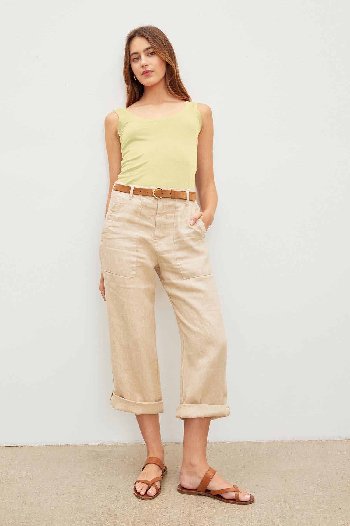   A woman stands posing in a Velvet by Graham & Spencer yellow MOSSY GAUZY WHISPER FITTED TANK, beige cropped pants with a belt, and brown sandals against a plain white background. 