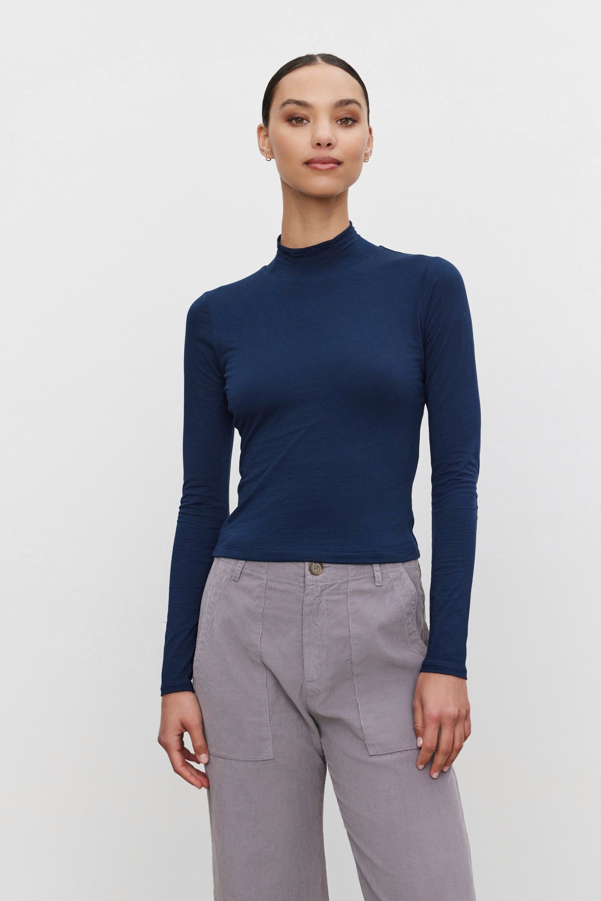   A person wearing the NADENE TEE from Velvet by Graham & Spencer paired with gray high-waisted pants, standing against a plain white background. 