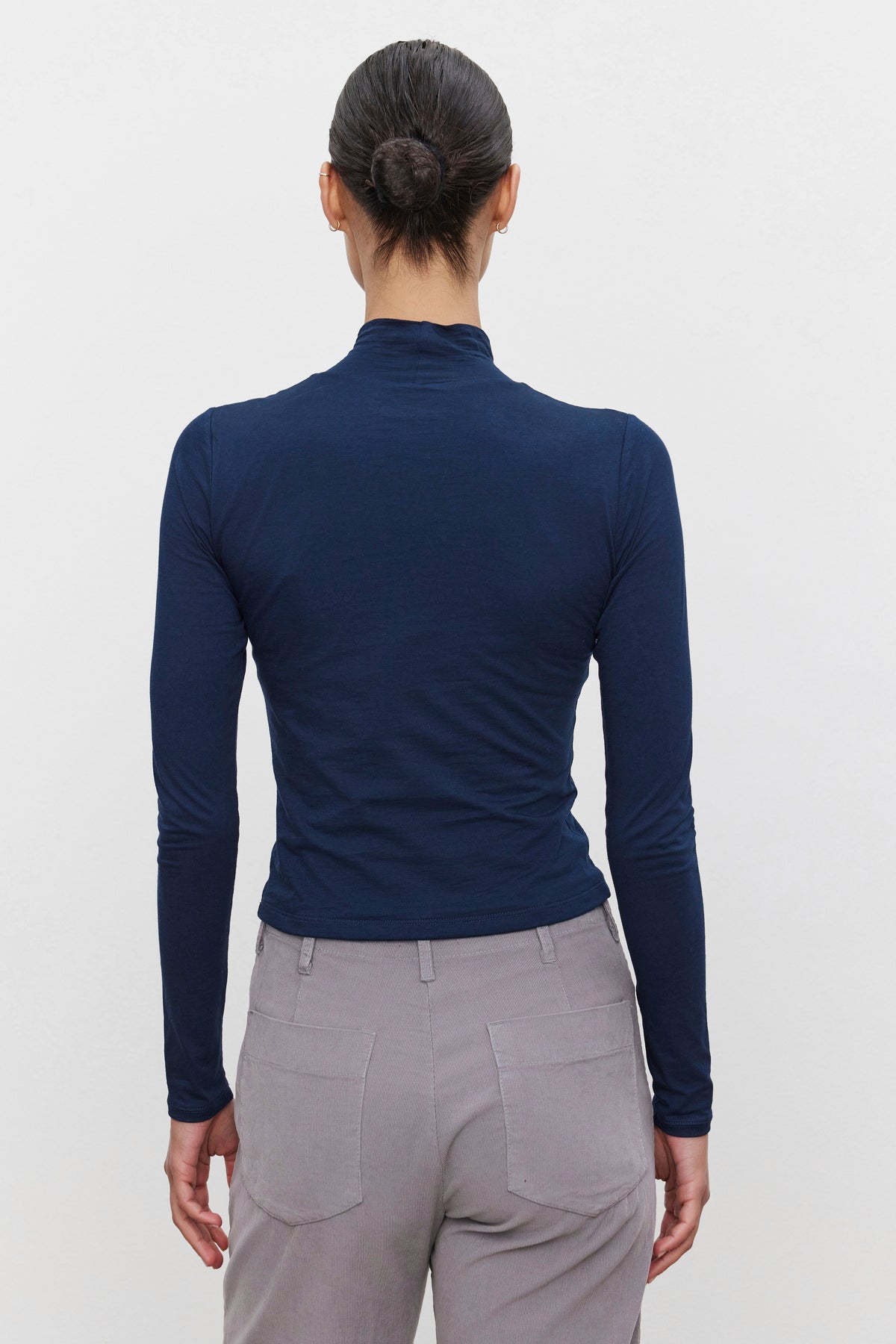   A person with hair in a bun is wearing the NADENE TEE by Velvet by Graham & Spencer, paired with gray pants, showcasing a sleek silhouette while facing away from the camera. 