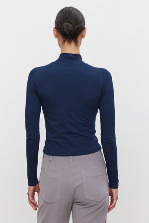 A person with hair in a bun is wearing the NADENE TEE by Velvet by Graham & Spencer, paired with gray pants, showcasing a sleek silhouette while facing away from the camera.