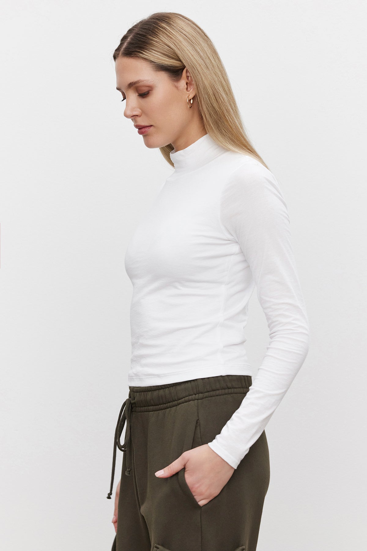   A woman with straight hair is wearing the NADENE TEE by Velvet by Graham & Spencer and olive green pants, standing in profile against a plain background. 