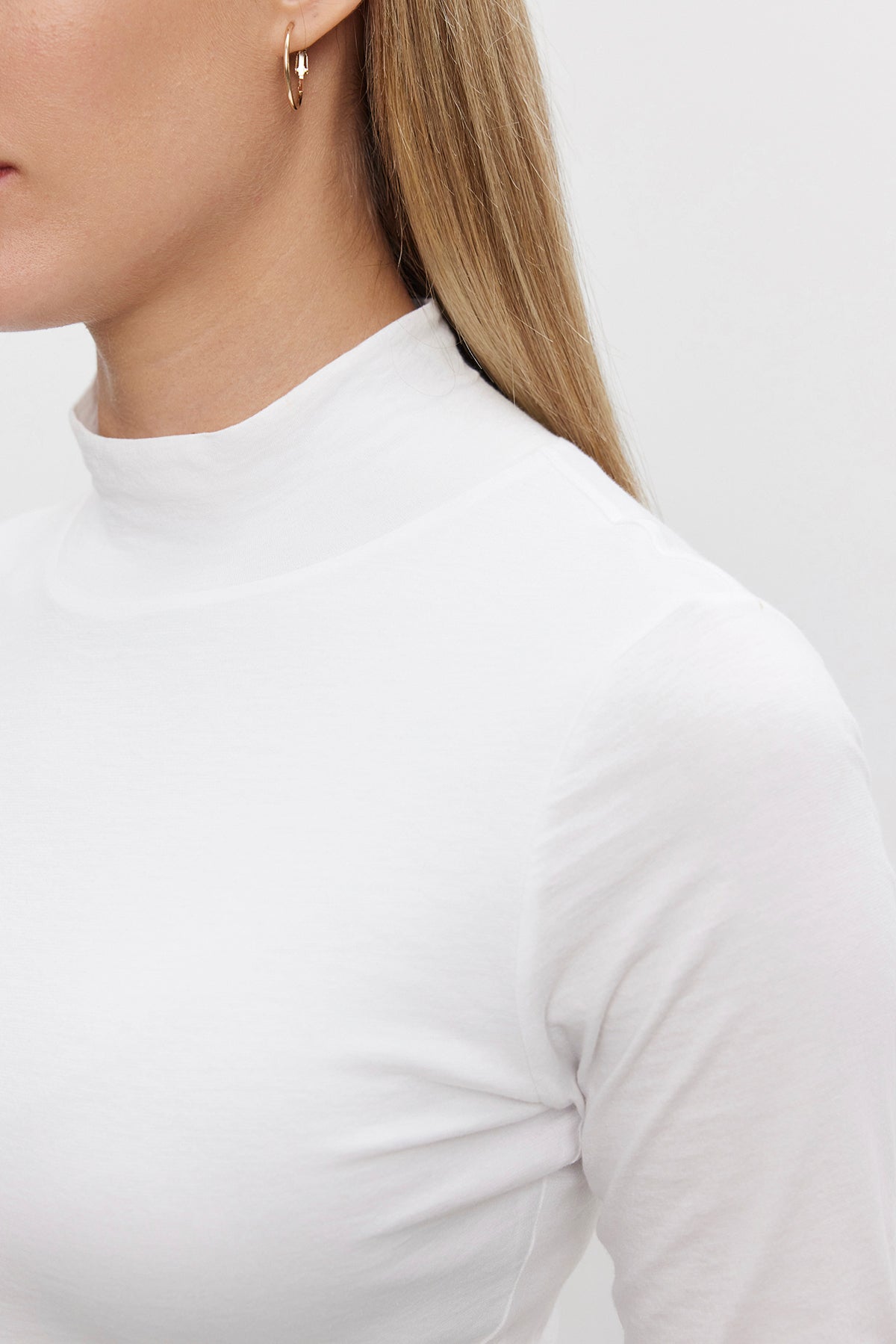   A person wearing the NADENE TEE from Velvet by Graham & Spencer and small hoop earrings, with long straight blonde hair, is shown in a side profile against a neutral background. 