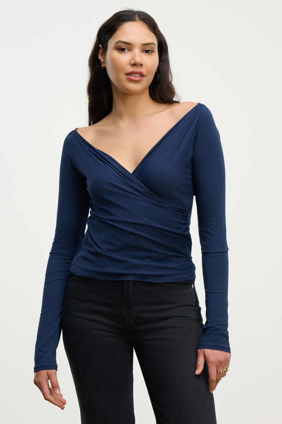   A woman faces the camera in a Velvet by Graham & Spencer RAK TEE, paired with black jeans against a light background, highlighting her feminine silhouette. 