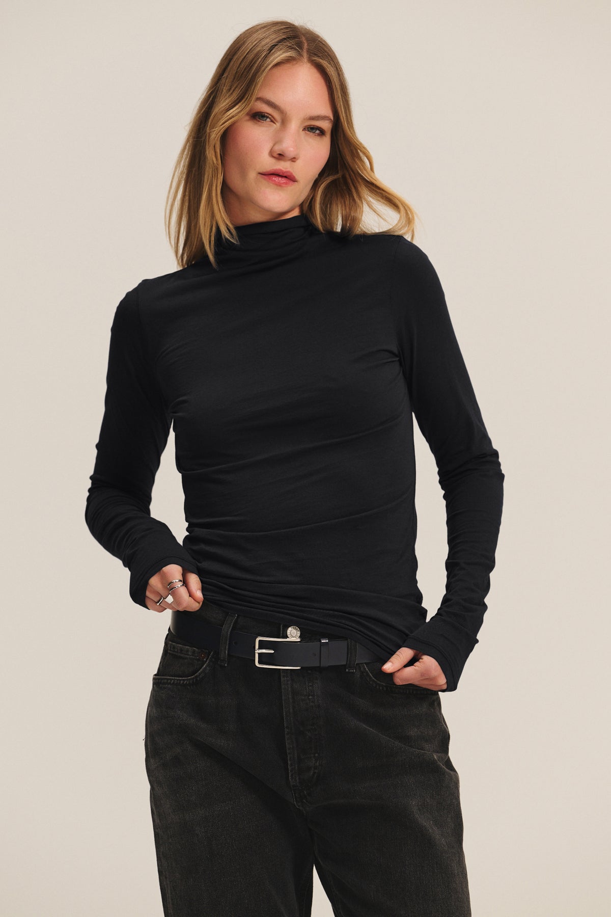 A woman wears the TALISIA TEE by Velvet by Graham & Spencer with black jeans and a black belt, standing against a plain light background, one hand in her pocket.-40182502195393