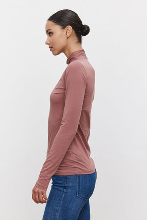 A woman with dark hair in a low bun is wearing the TALISIA TEE by Velvet by Graham & Spencer and blue jeans, posed in profile against a plain white background.