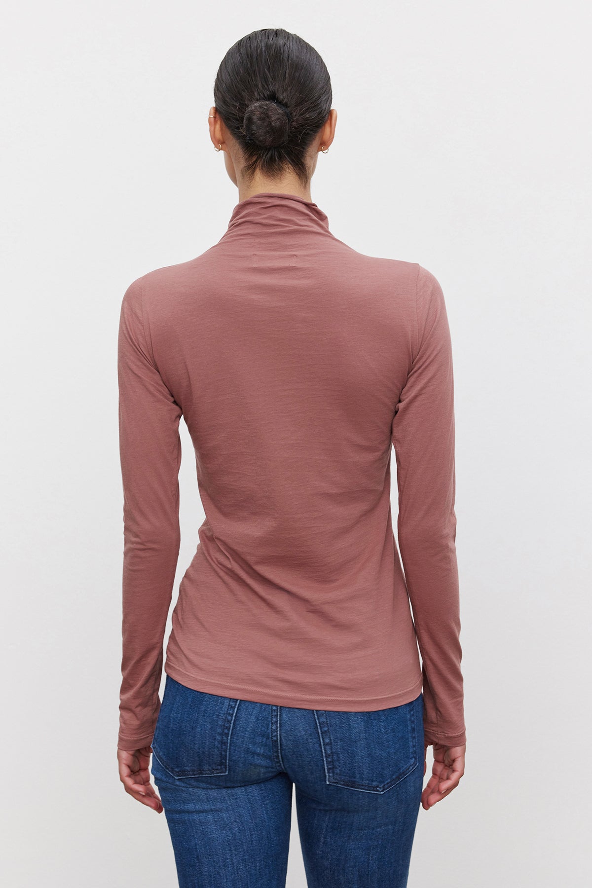   A person with dark hair in a bun is wearing the TALISIA TEE by Velvet by Graham & Spencer along with blue jeans, facing away from the camera. 