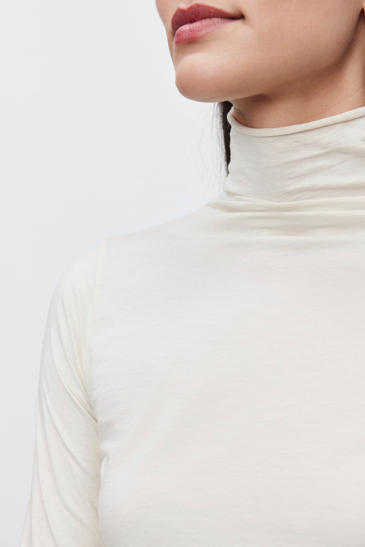   Close-up of a person wearing the TALISIA TEE by Velvet by Graham & Spencer, showcasing this versatile wardrobe staple. The face is partially visible, focusing mainly on the lips and neck area. The background is plain and light-colored. 