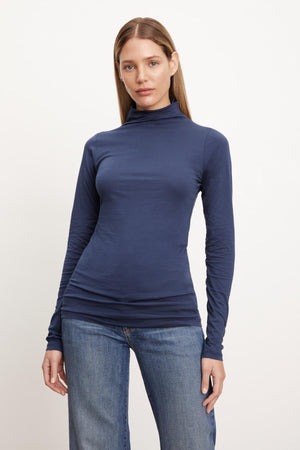 A woman showcasing a fashion-forward TALISIA GAUZY WHISPER FITTED MOCK NECK TEE by Velvet by Graham & Spencer, paired effortlessly with comfortable jeans - a perfect wardrobe staple.