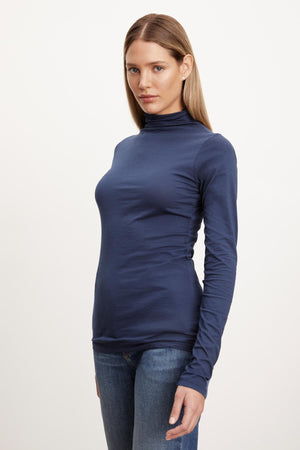 A woman wearing a Velvet by Graham & Spencer TALISIA GAUZY WHISPER FITTED MOCK NECK TEE in blue, and jeans, showcasing a wardrobe staple.