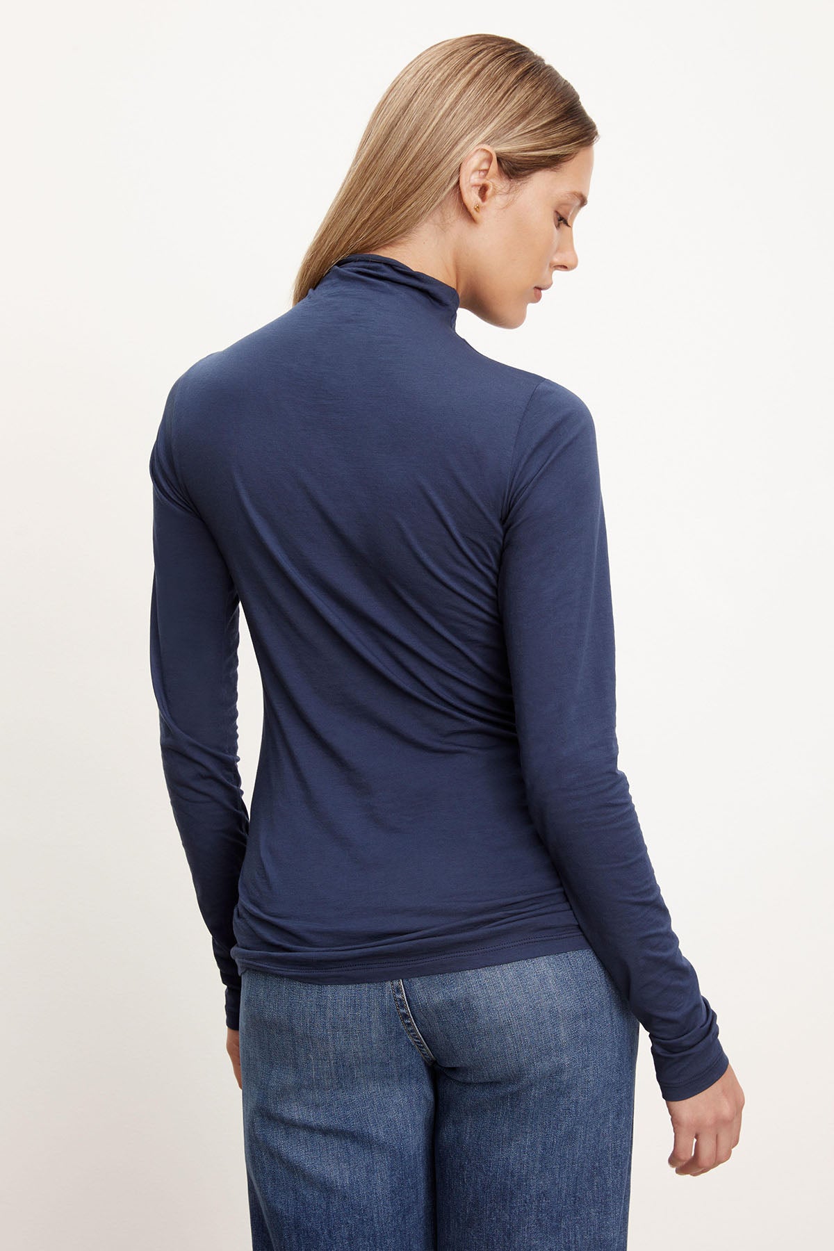 The back view of a woman sporting a fashionable outfit with jeans and the Velvet by Graham & Spencer TALISIA GAUZY WHISPER FITTED MOCK NECK TEE, making it a versatile wardrobe staple.-26895434285249
