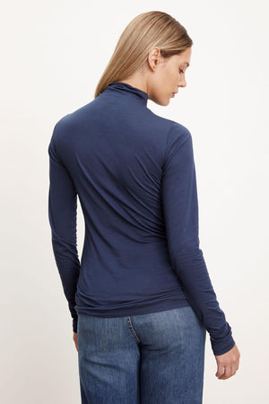 The back view of a woman sporting a fashionable outfit with jeans and the Velvet by Graham & Spencer TALISIA GAUZY WHISPER FITTED MOCK NECK TEE, making it a versatile wardrobe staple.