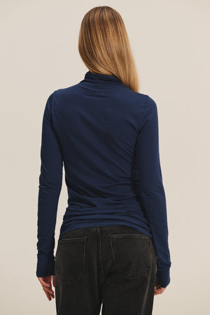 A person with long, straight hair wears the TALISIA TEE by Velvet by Graham & Spencer in navy blue, paired with black jeans and shown from the back against a plain background—an effortlessly chic wardrobe staple.
