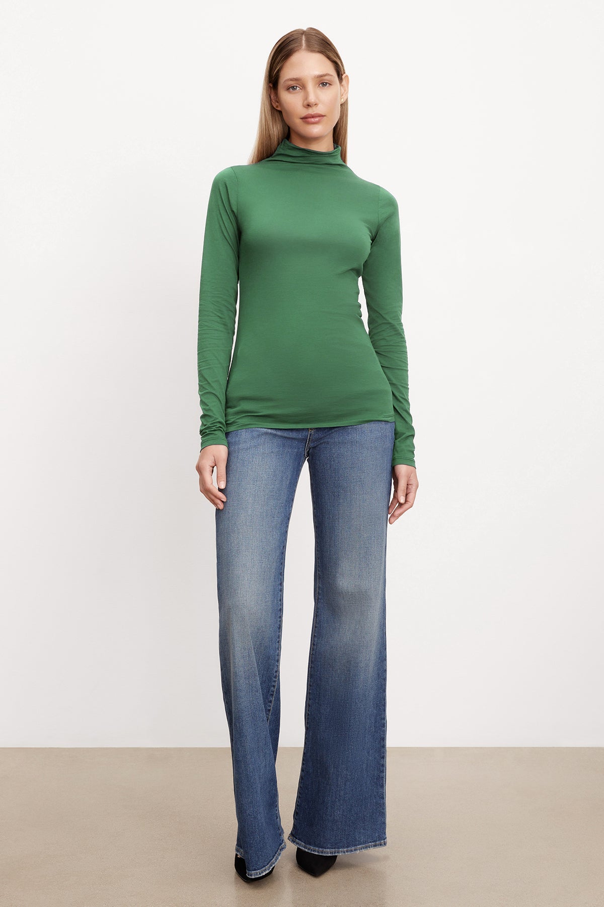 A woman donning a trendy TALISIA GAUZY WHISPER FITTED MOCK NECK TEE by Velvet by Graham & Spencer and flared jeans, showcasing her fashion world prowess.-36001491288257