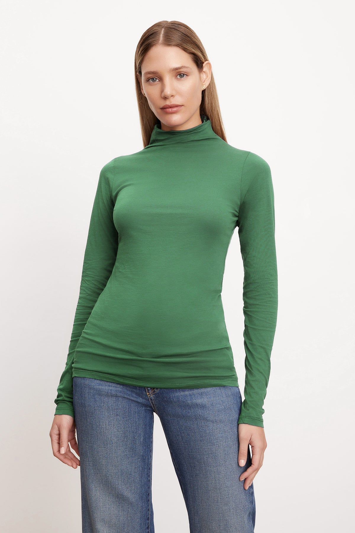   A woman donning a green Velvet by Graham & Spencer TALISIA GAUZY WHISPER FITTED MOCK NECK TEE, a wardrobe staple in the fashion world. She pairs it with jeans for a casually chic look. 