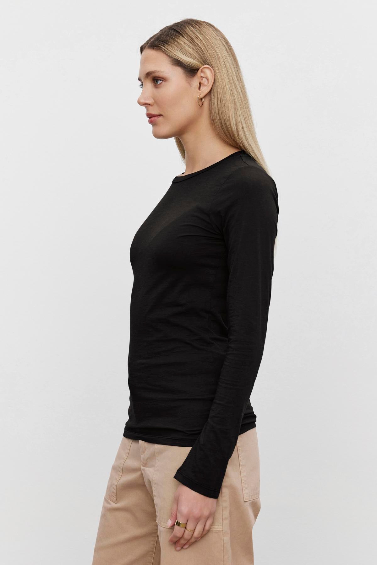 A person with long blonde hair is seen in profile, wearing the ultra-soft gauzy whisper black ZOFINA TEE by Velvet by Graham & Spencer and light-colored pants. The background is plain white.-37648649945281