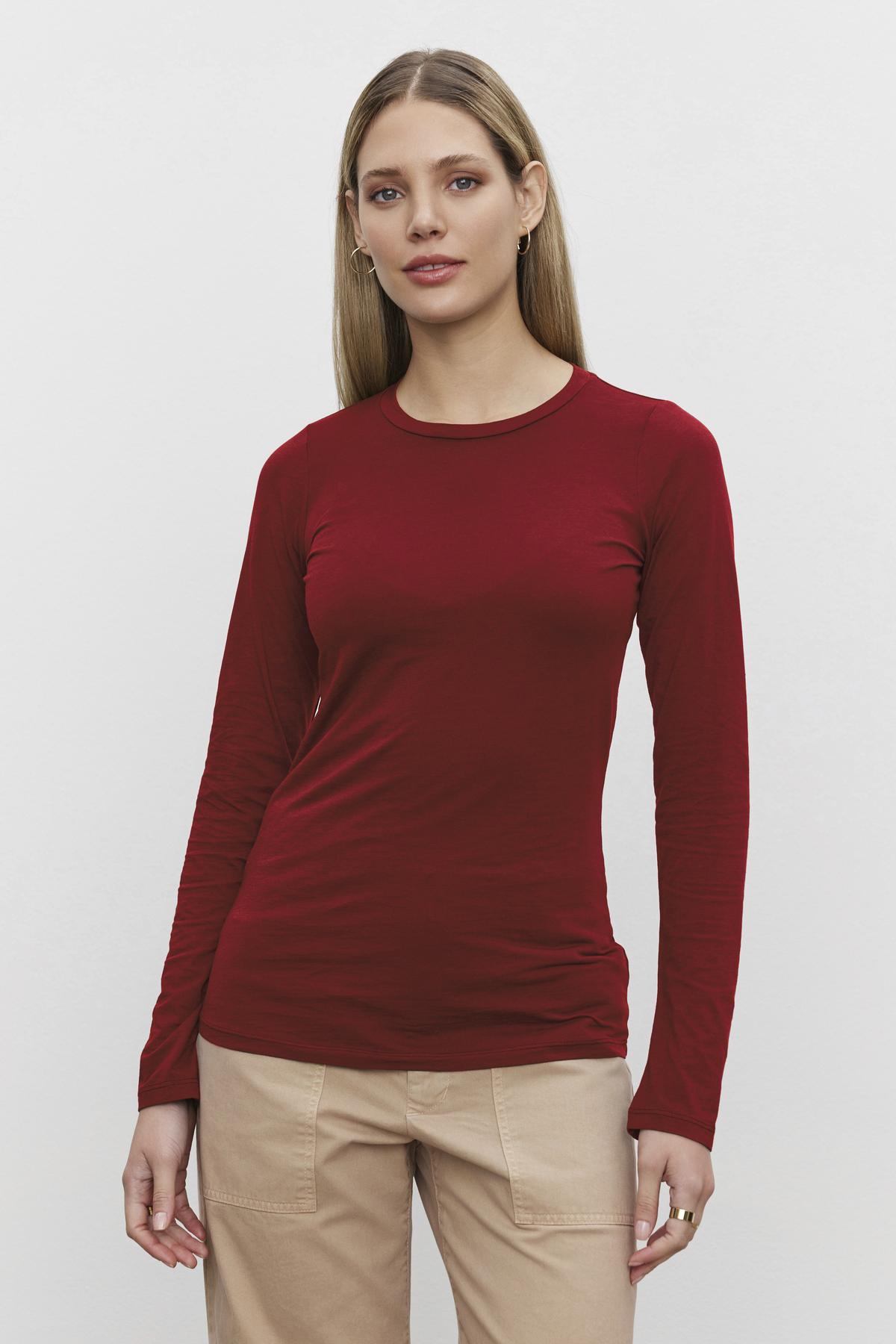   A person with long hair is wearing a red ZOFINA TEE from Velvet by Graham & Spencer made from ultra-soft gauzy whisper fabrication and beige pants, standing against a plain white background. 