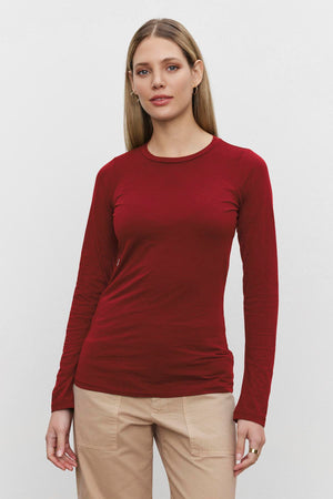 A person with long hair is wearing a red ZOFINA TEE from Velvet by Graham & Spencer made from ultra-soft gauzy whisper fabrication and beige pants, standing against a plain white background.