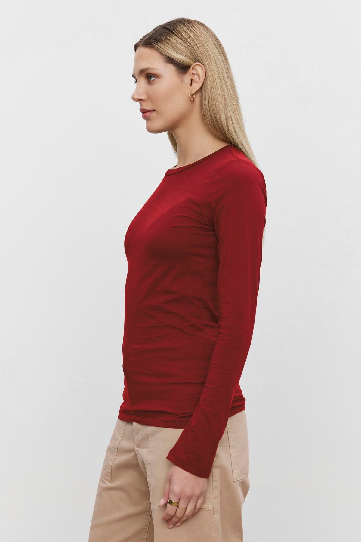   A woman with long blonde hair wears the Velvet by Graham & Spencer ZOFINA TEE in red and beige pants, standing in profile against a plain white background. The ultra-soft gauzy whisper fabrication of the shirt enhances its appeal. 