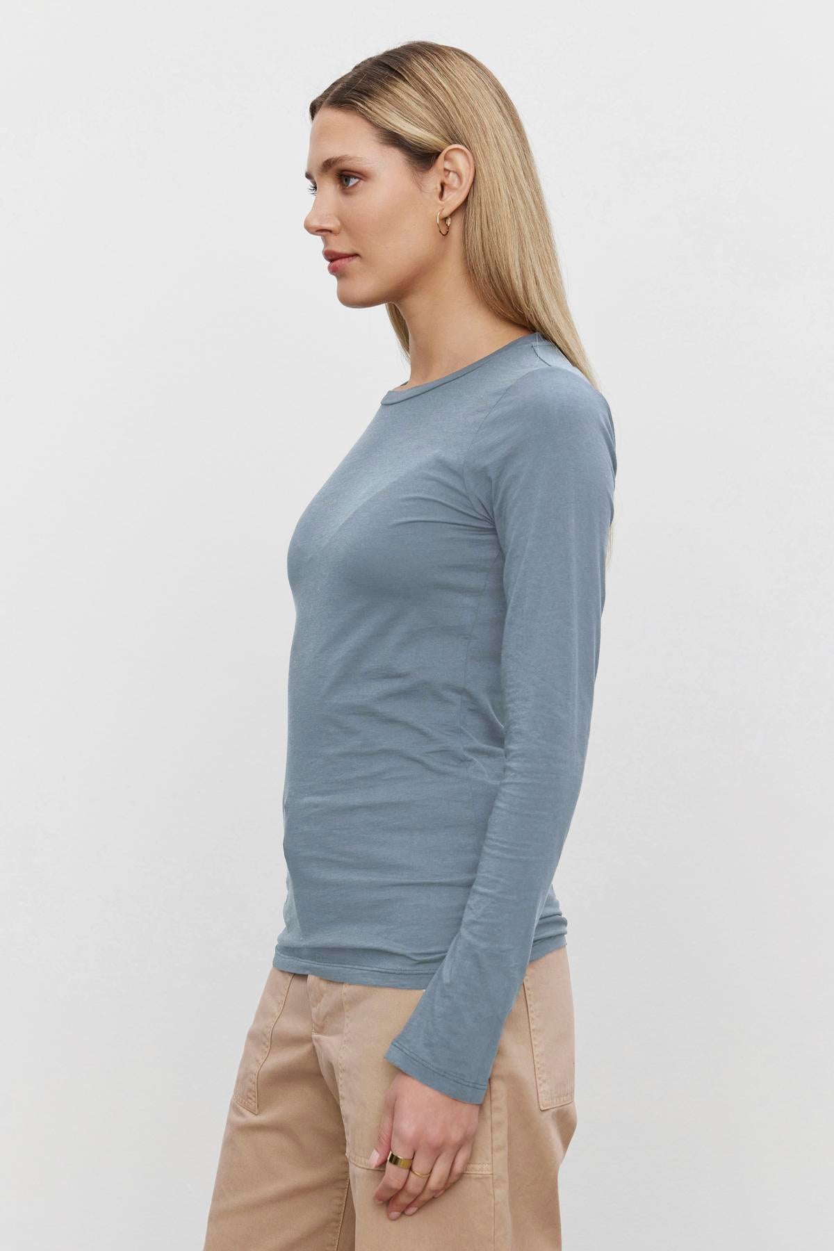   A woman standing sideways, wearing the ZOFINA TEE from Velvet by Graham & Spencer in light blue and beige pants against a plain white background. 