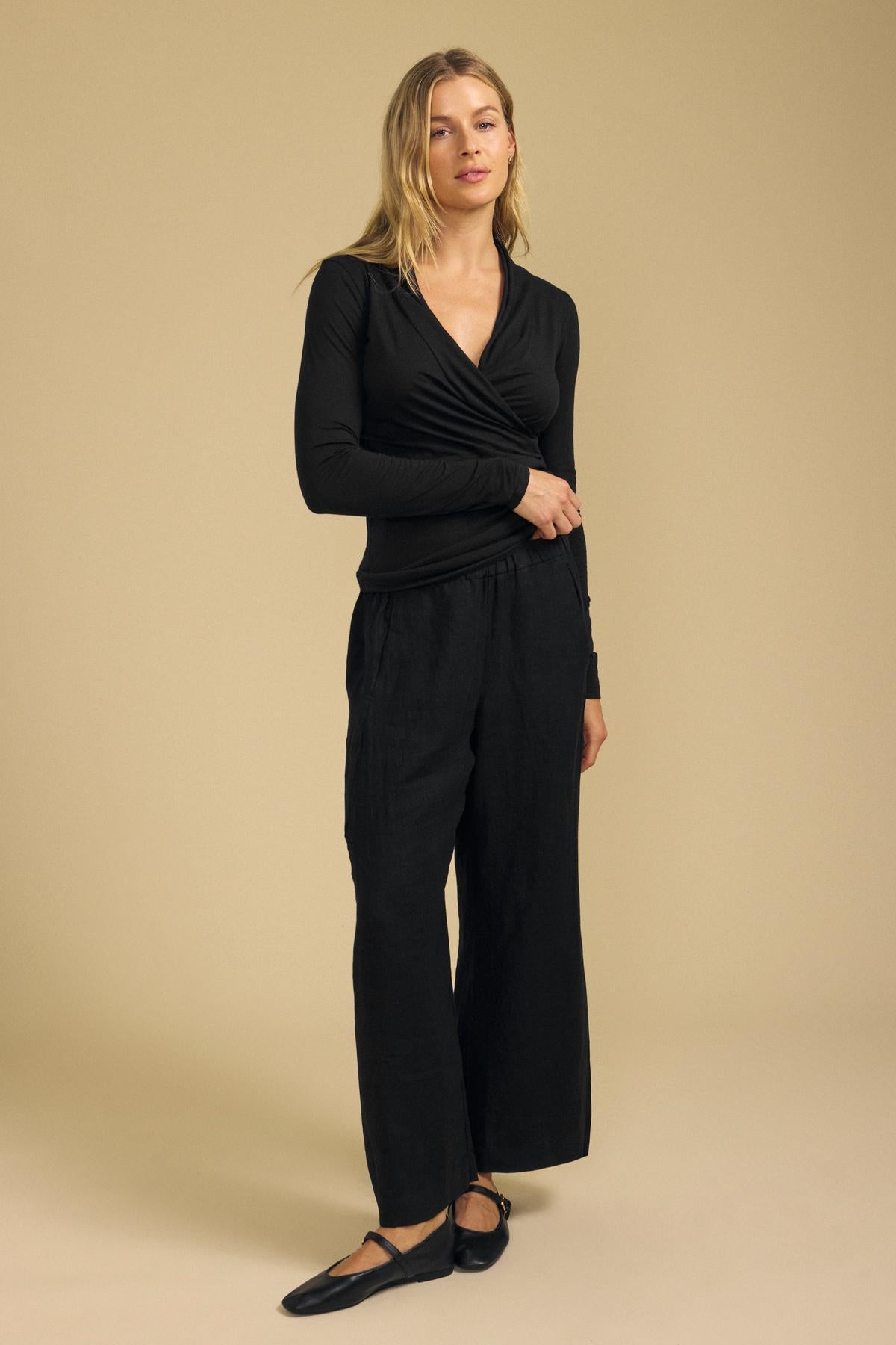 Front view of the fitted black MERI TEE showcasing its wrap front and V-neck on a model against a beige background