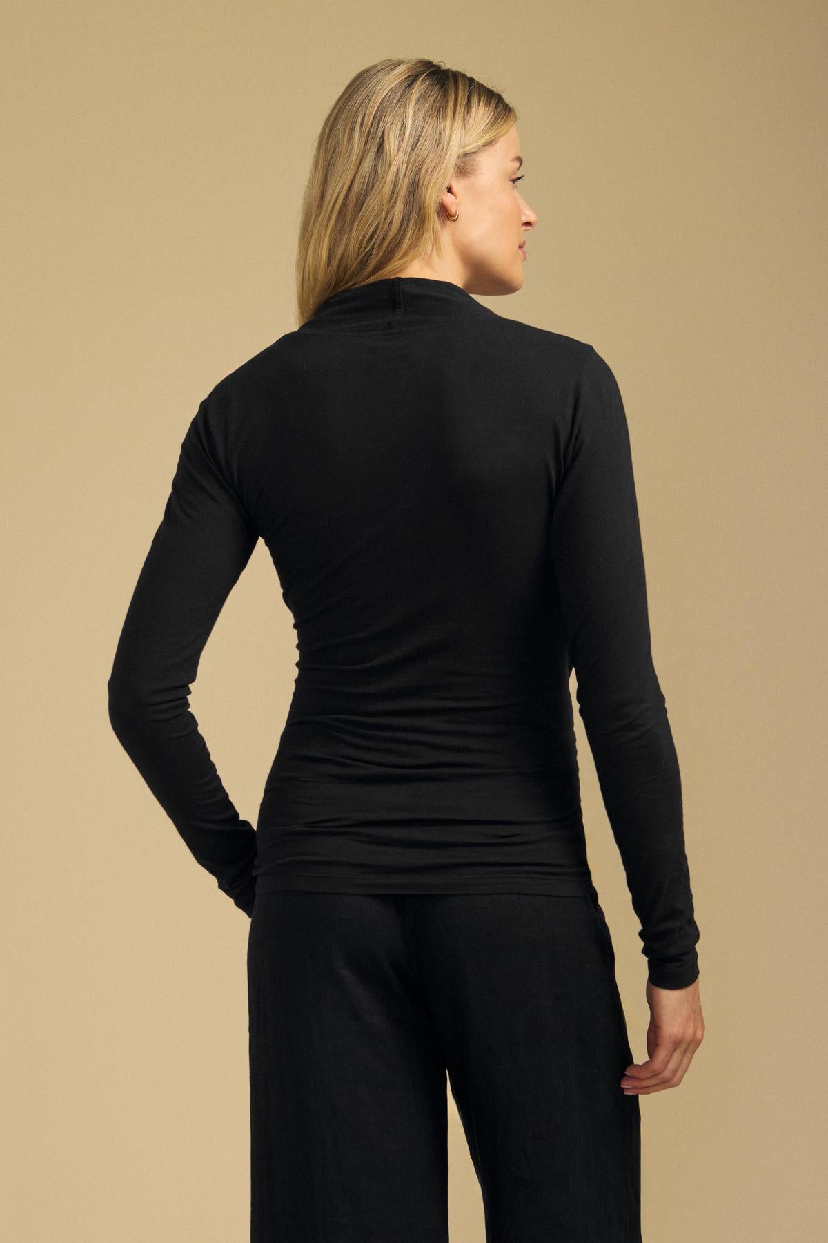 Back view of the black MERI Gauzy Whisper wrap tee showcasing its fitted long sleeves against a beige background