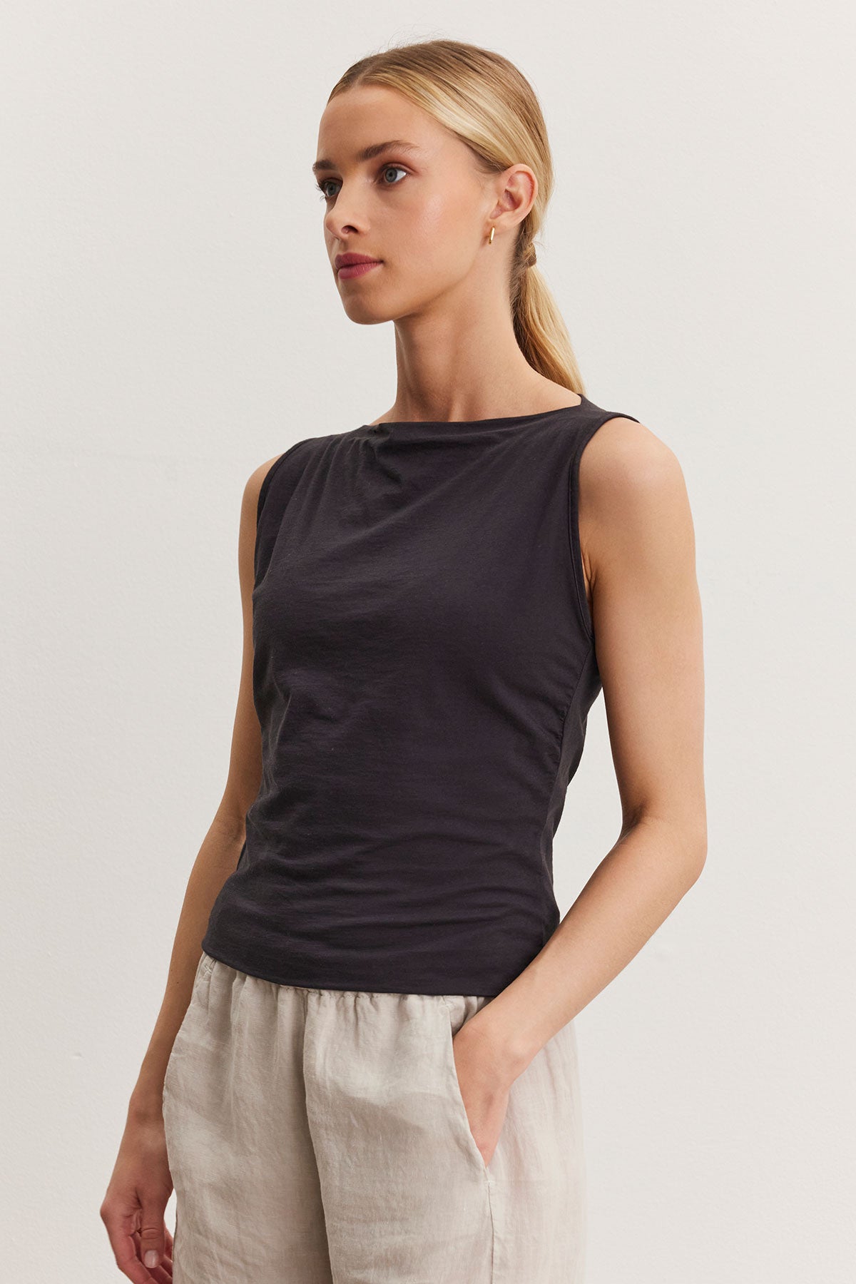   A woman wearing a Velvet by Graham & Spencer EMILIA tank top and light linen pants, standing against a plain white background. 