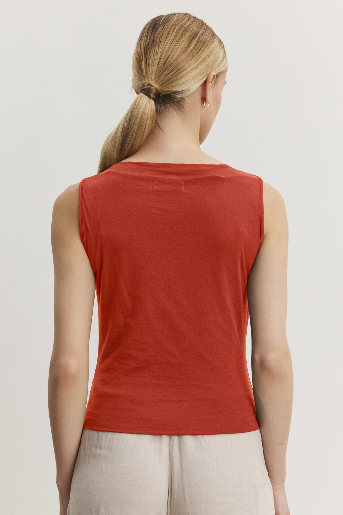   A person with blond hair tied in a low ponytail is shown from the back, wearing a Velvet by Graham & Spencer EMILIA TANK TOP and beige pants. 