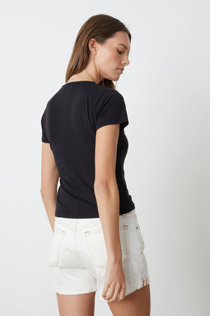 The back view of a person wearing Velvet by Graham & Spencer Natalie rolled hem shorts and a cut-off black t-shirt.