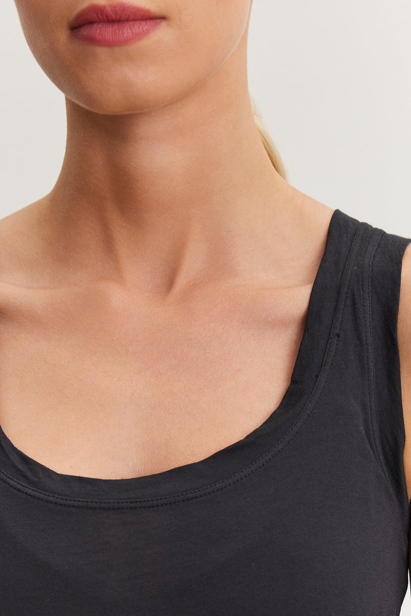 Close-up of a person wearing a versatile wardrobe staple: a sleeveless black MOSSY TANK TOP by Velvet by Graham & Spencer, showing their neck, shoulder, and part of their face.